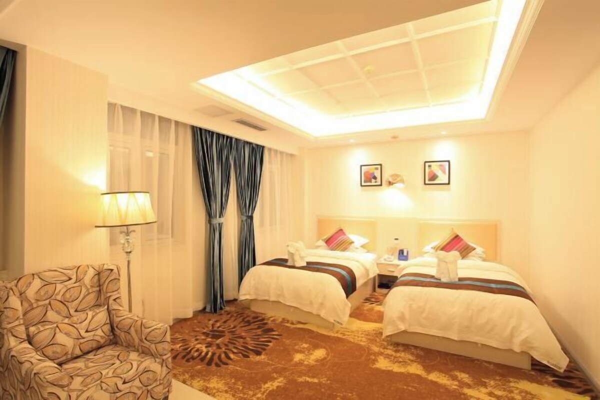 A hotel room with two beds, a chair, a lamp, and a ceiling light.