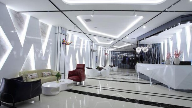 A modern lobby with a sleek design, featuring a reception desk, seating area with a sofa and chairs, and a decorative wall with abstract patterns.