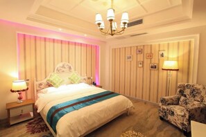 A hotel room with a large bed, a nightstand, a chair, and a wall with pictures. - Anlong Aishang Boutique Hotel (Anlong)
