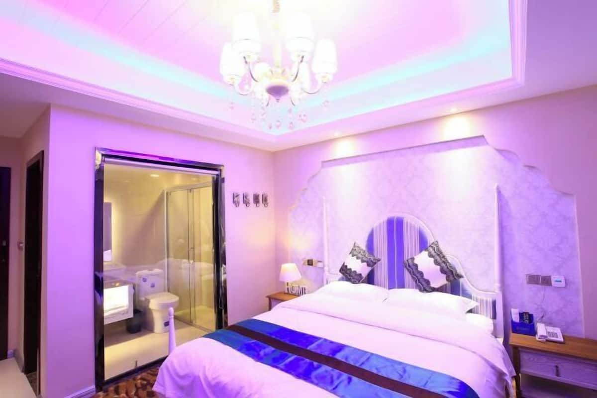 Ein Hotelzimmer mit Bett, einer gläsernen Dusche, einem Chandelier und einem wandmontierten Spiegel.