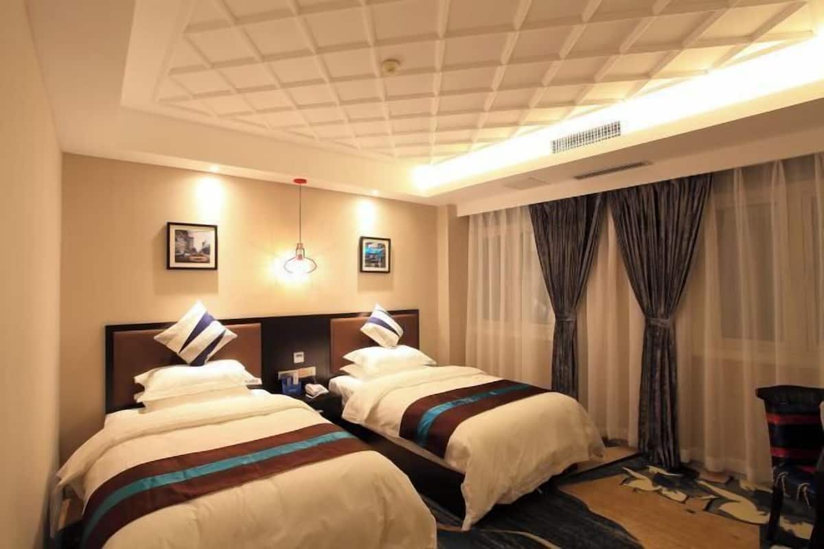 Ein Hotelzimmer mit zwei Betten, einer Deckenleuchte, einem an der Wand montierten Telefon und einem Fenster mit Vorhängen.