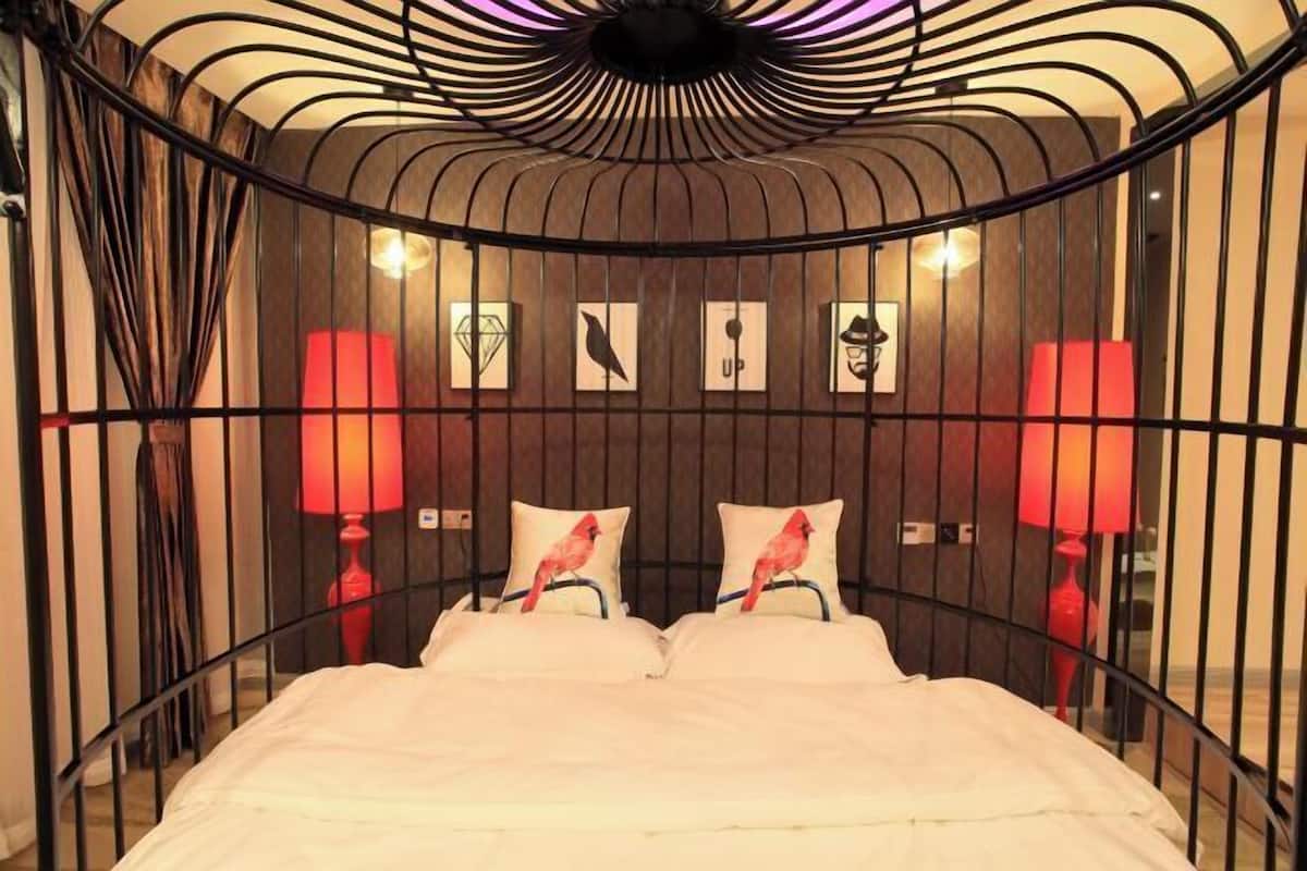 Ein Bett mit gebogenem Metallgestell, zwei rote Lampen und Wandkunst, darunter ein Vogel und geometrische Formen.
