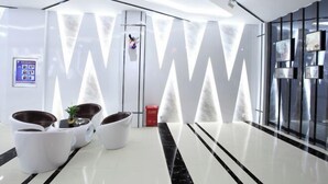 A modern lobby with a glass wall, seating area, and a digital information board.