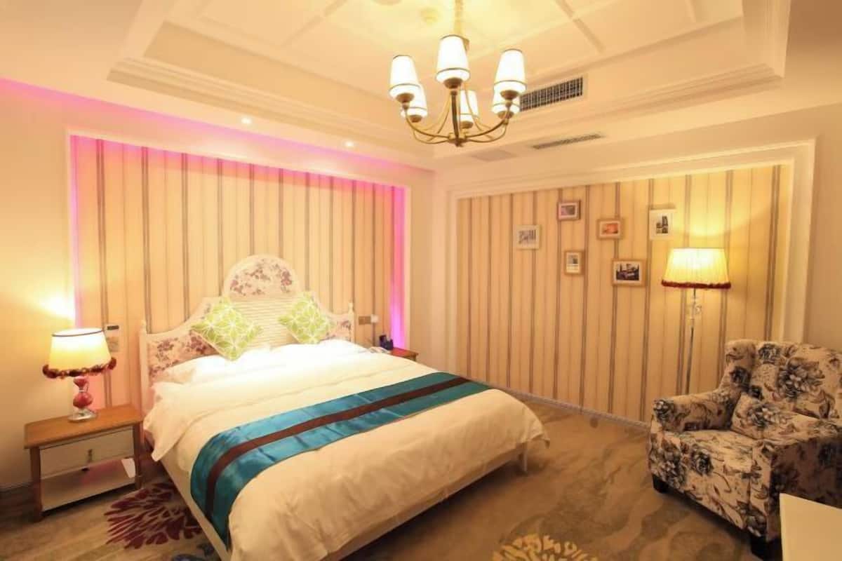 Ein Hotelzimmer mit einem Bett, einem Sessel, einem Nachttisch, einer Lampe und einer Wand mit gerahmten Bildern.