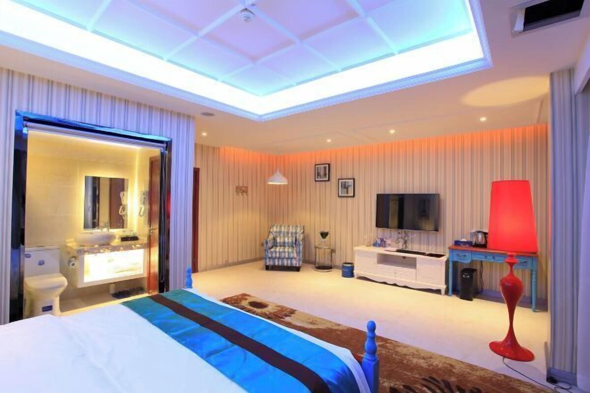 A modern hotel room with a large bed, a television, a desk, and a red lamp.