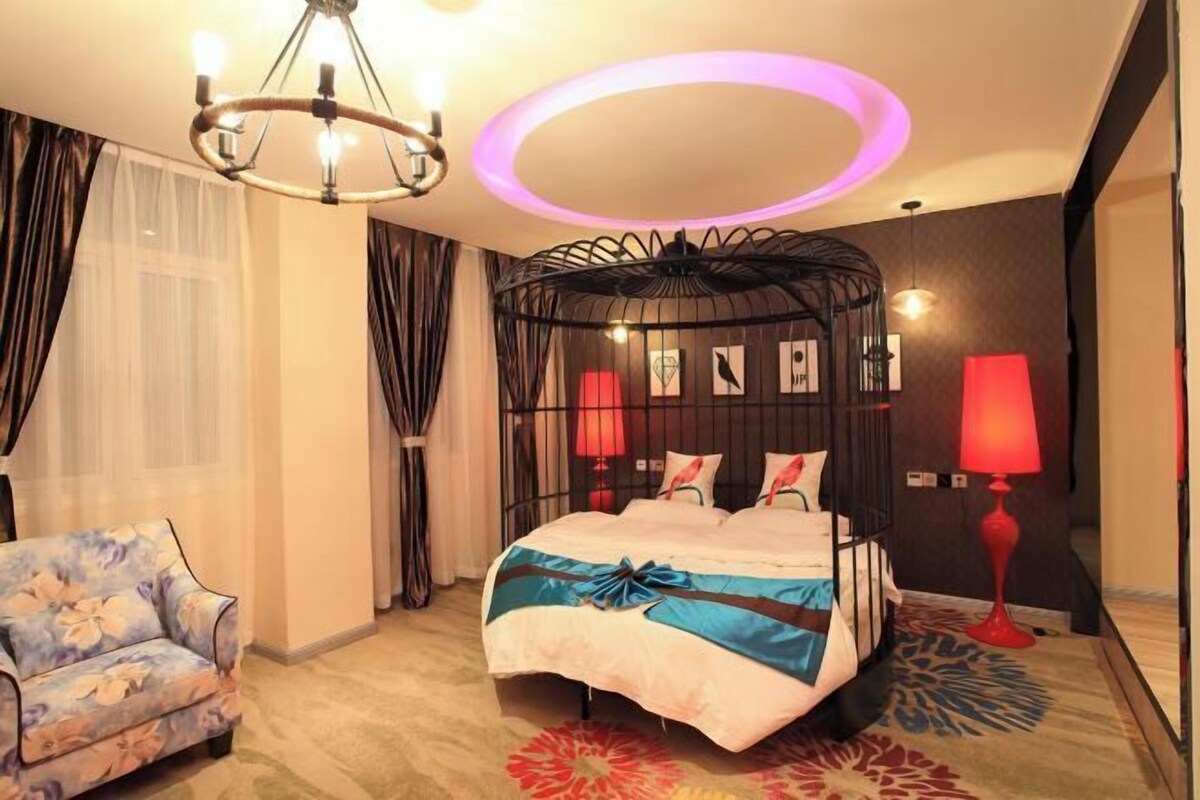 A hotel room with a bed, a chair, a circular ceiling light, and a wall-mounted lamp.