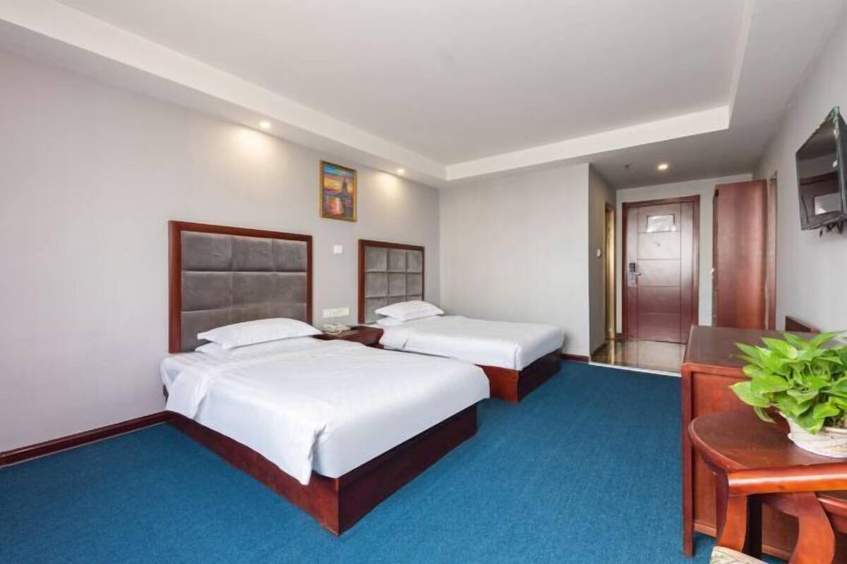 Habitación de hotel con dos camas, un escritorio, una silla, un televisor y una puerta.