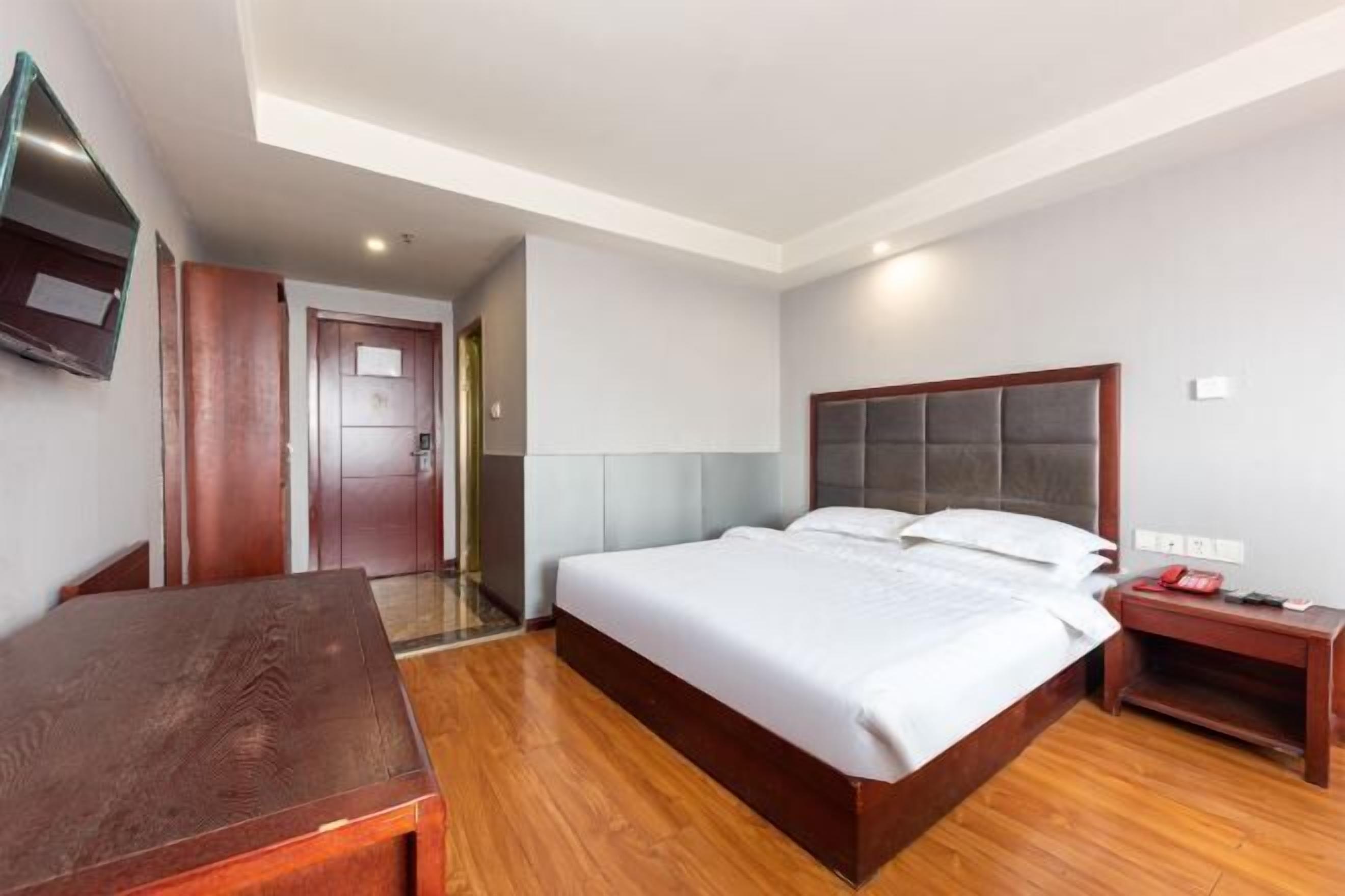 A bedroom with a bed, wooden desk, and a TV mounted on the wall.