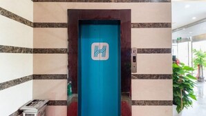 Un ascensor azul con un logotipo, rodeado de paredes de mármol a rayas y un acceso alfombrado en rojo.