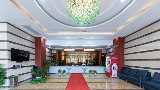 Un vestíbulo de hotel con alfombra roja, un mostrador de recepción, una araña y un sofá.