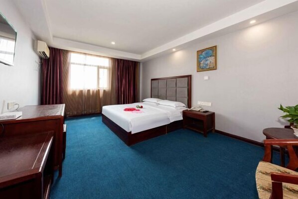 Habitación de hotel con una cama grande, un escritorio, una silla, una mesita de noche y un ventanal con cortinas.