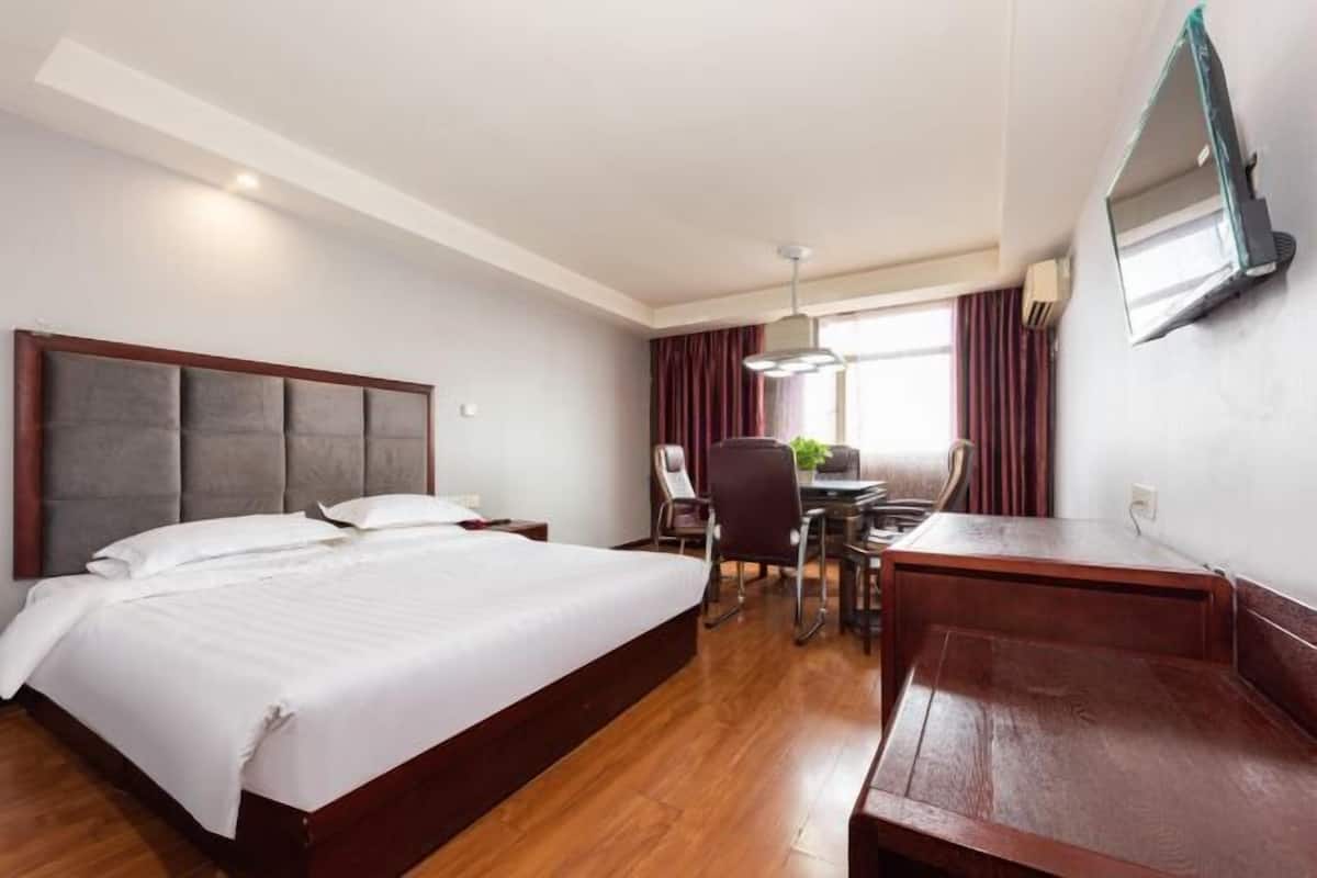 Habitación de hotel con una cama grande, un escritorio, una silla y un televisor montado en la pared.