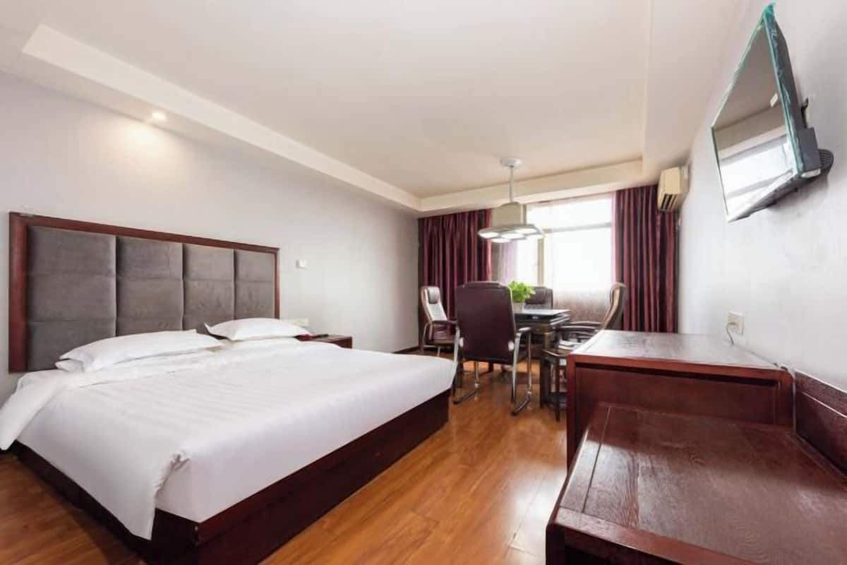 Una habitación de hotel con una cama grande, un escritorio con silla y un televisor montado en la pared.