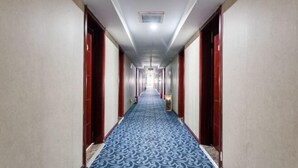 Un largo y estrecho pasillo de hotel con alfombra estampada, puertas de madera y un respiradero en el techo.