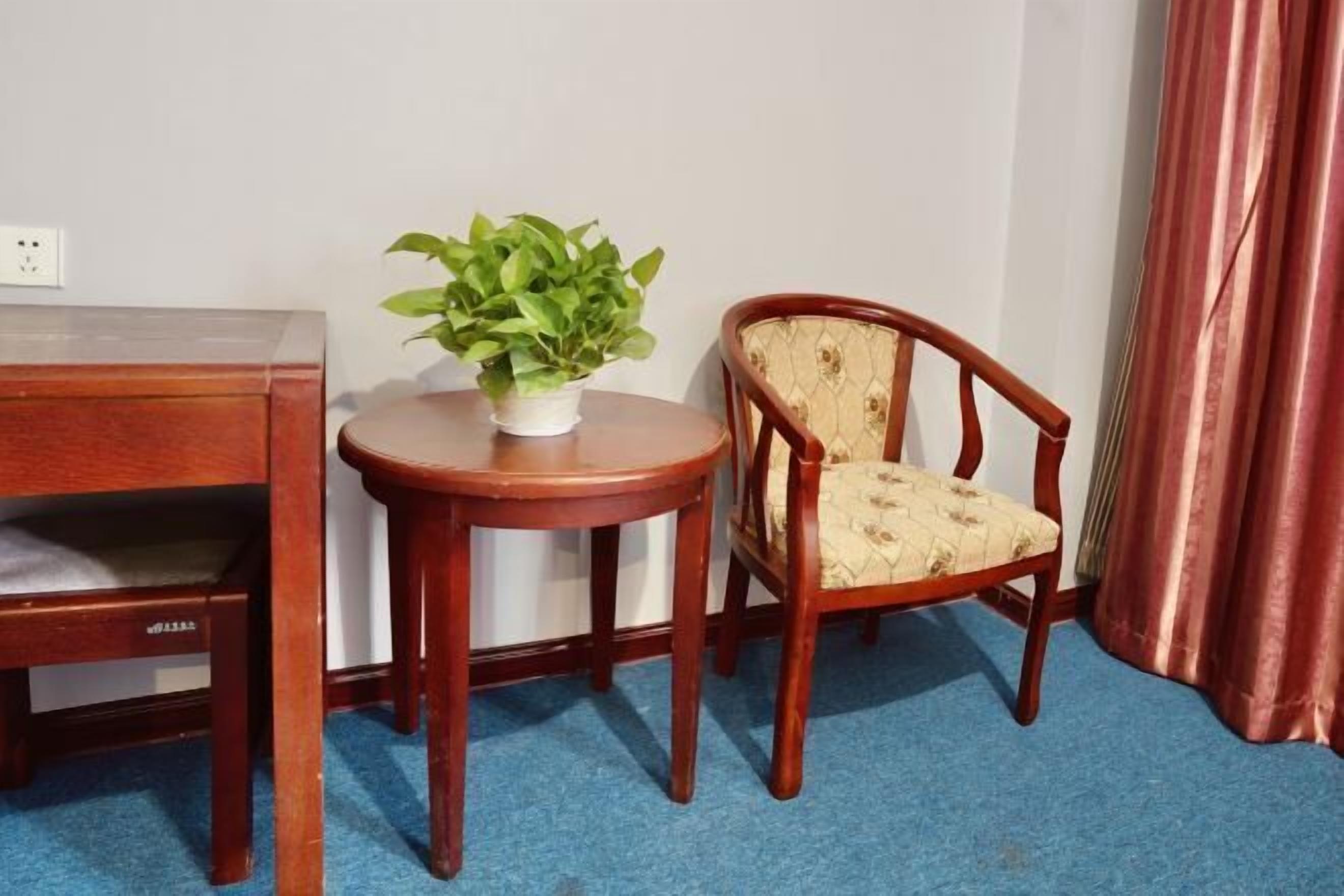 A wooden desk, a round table with a potted plant, and a cushioned chair in a room with a blue carpet.