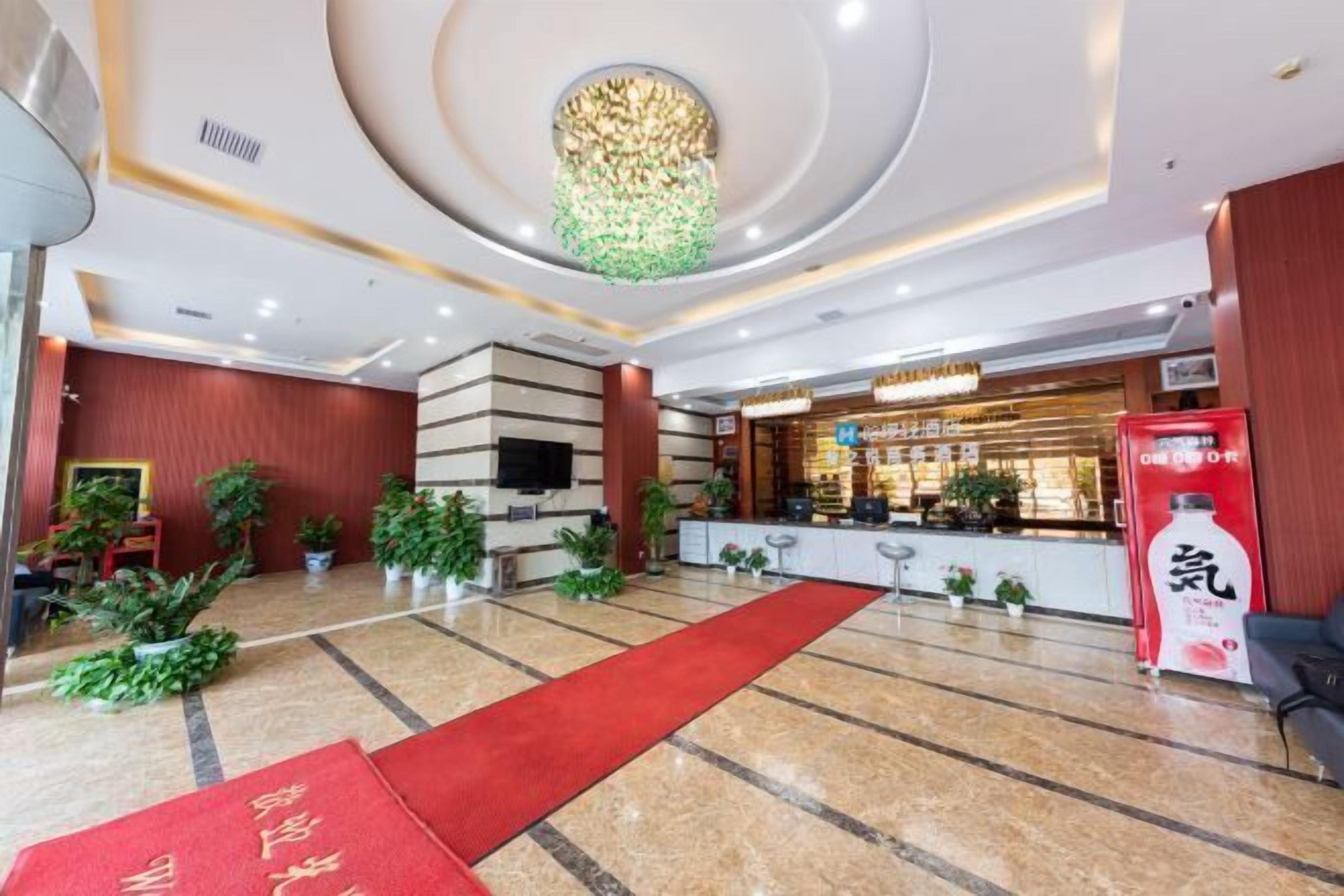 A hotel lobby with a red carpet, a reception desk, and a large plant in the center.