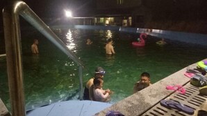 A swimming pool area with a metal ladder, a few people in the water, and inflatable toys. - Yu Shan Hua Ting Holiday Hotel (Pingjiang)