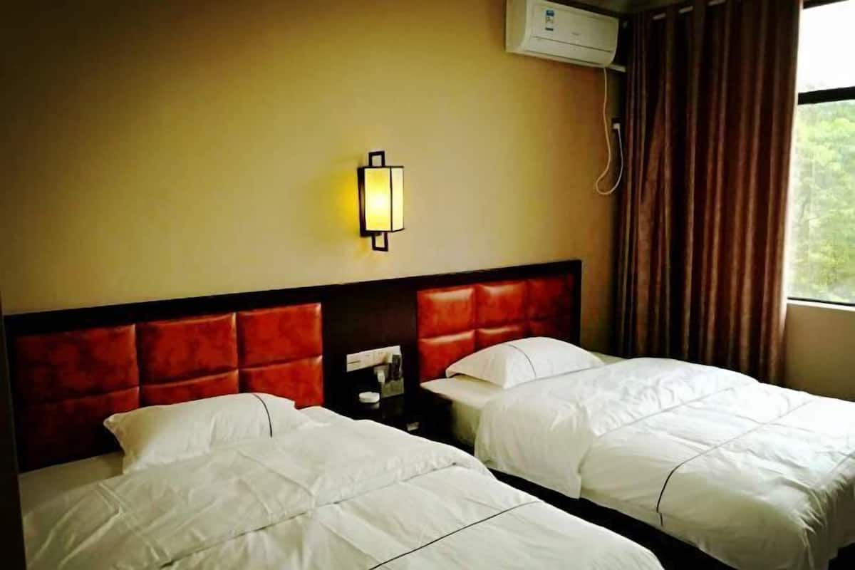Ein Hotelzimmer mit zwei Betten, einem roten Kopfteil, einer Wandleuchte und einer Klimaanlage.