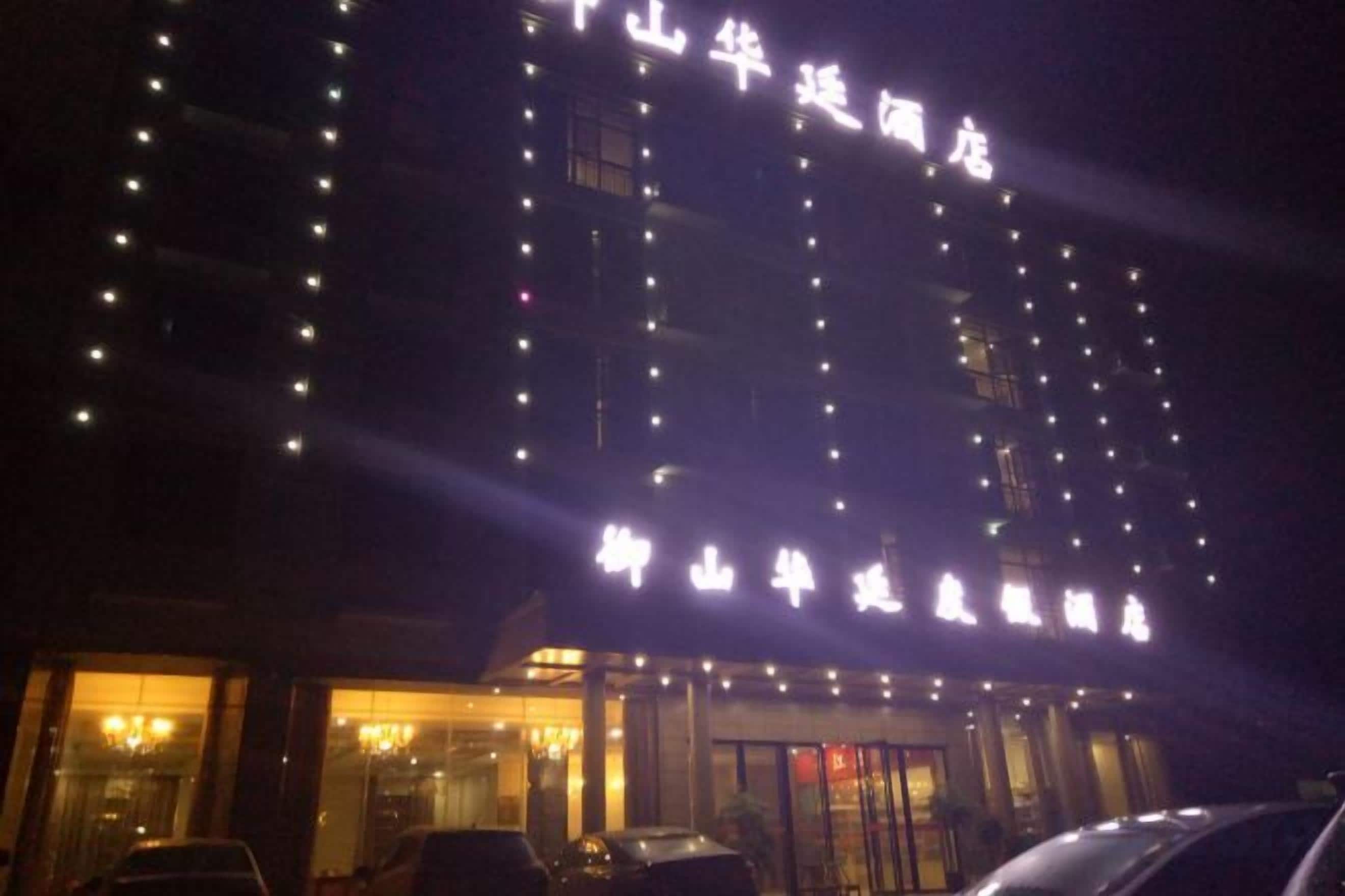 A multi-story building with illuminated signage, a glass entrance, and parked cars in front.