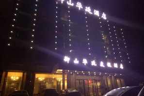 A multi-story building with illuminated signage, a glass entrance, and parked cars in front.
