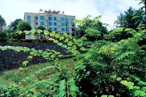 A building with a stone wall and dense foliage in the foreground. - Yu Shan Hua Ting Holiday Hotel (Pingjiang)