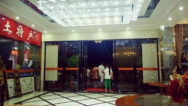 A hotel entrance with a glass door, a red sign with white text, and a chandelier above. - Yu Shan Hua Ting Holiday Hotel (Pingjiang)