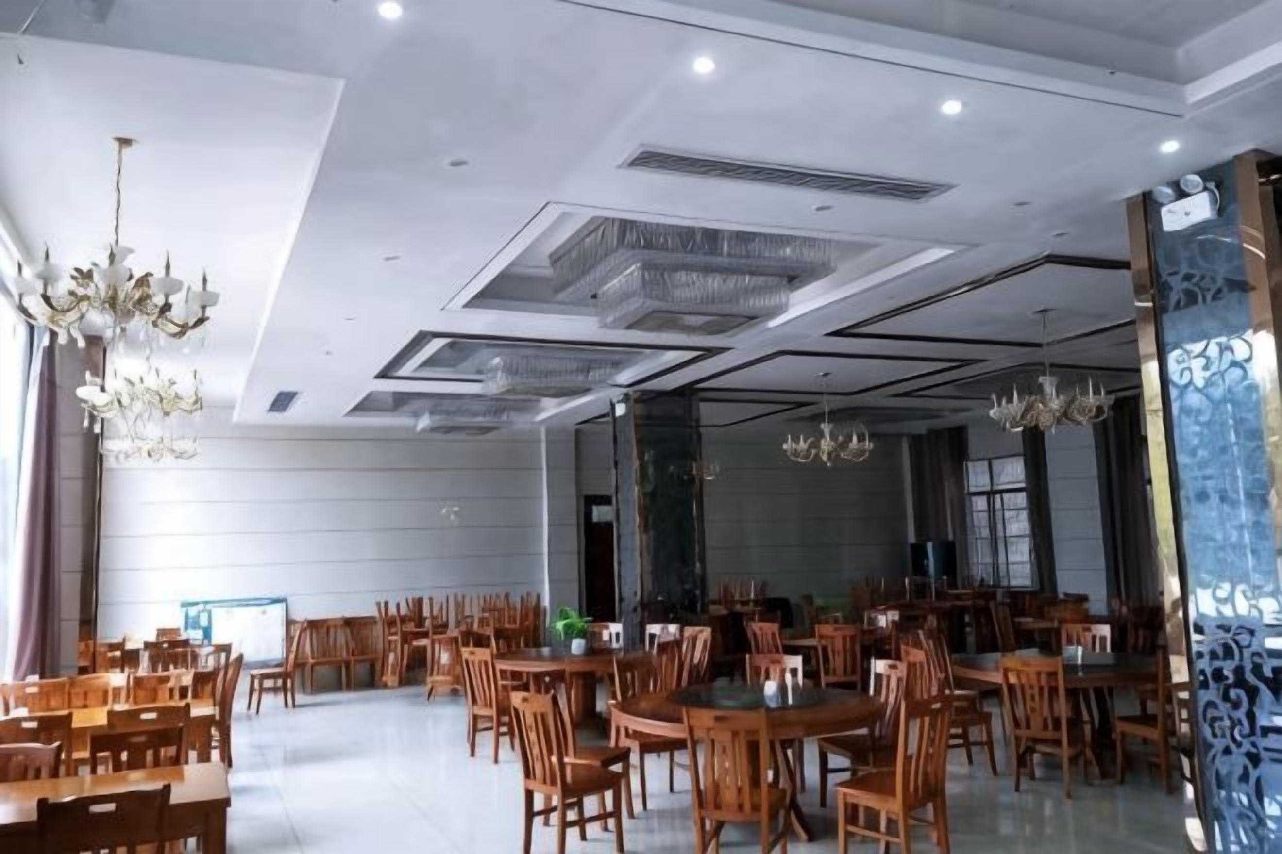 A spacious dining area with multiple tables and chairs, a chandelier, and a modern ceiling design.