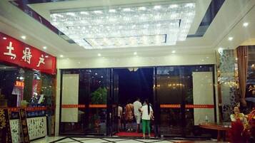 A hotel lobby with a glass entrance, a red sign on the left, and a chandelier above.