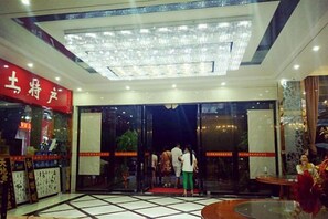 A hotel lobby with a glass entrance, a red sign on the left, and a chandelier above.