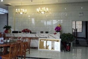 A hotel lobby with a marble reception desk, wooden chairs, a chandelier, potted plants, and a display board. - Yu Shan Hua Ting Holiday Hotel (Pingjiang)