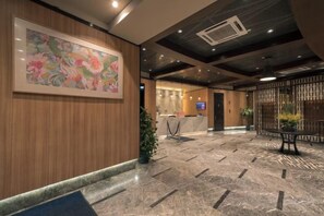 Een hotel lobby met een receptiebalie, een groot bloemschilderij, een plant en een vloerkleed met zebrapatroon.