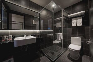 A modern bathroom with a glass-enclosed shower, a white sink, and a toilet.