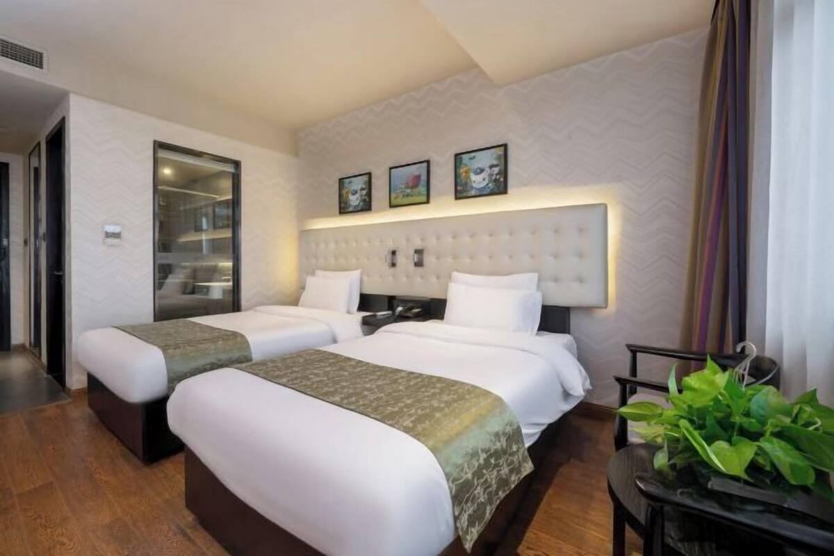 A hotel room with two beds, a large padded headboard, a small table with a plant, and a mirror.