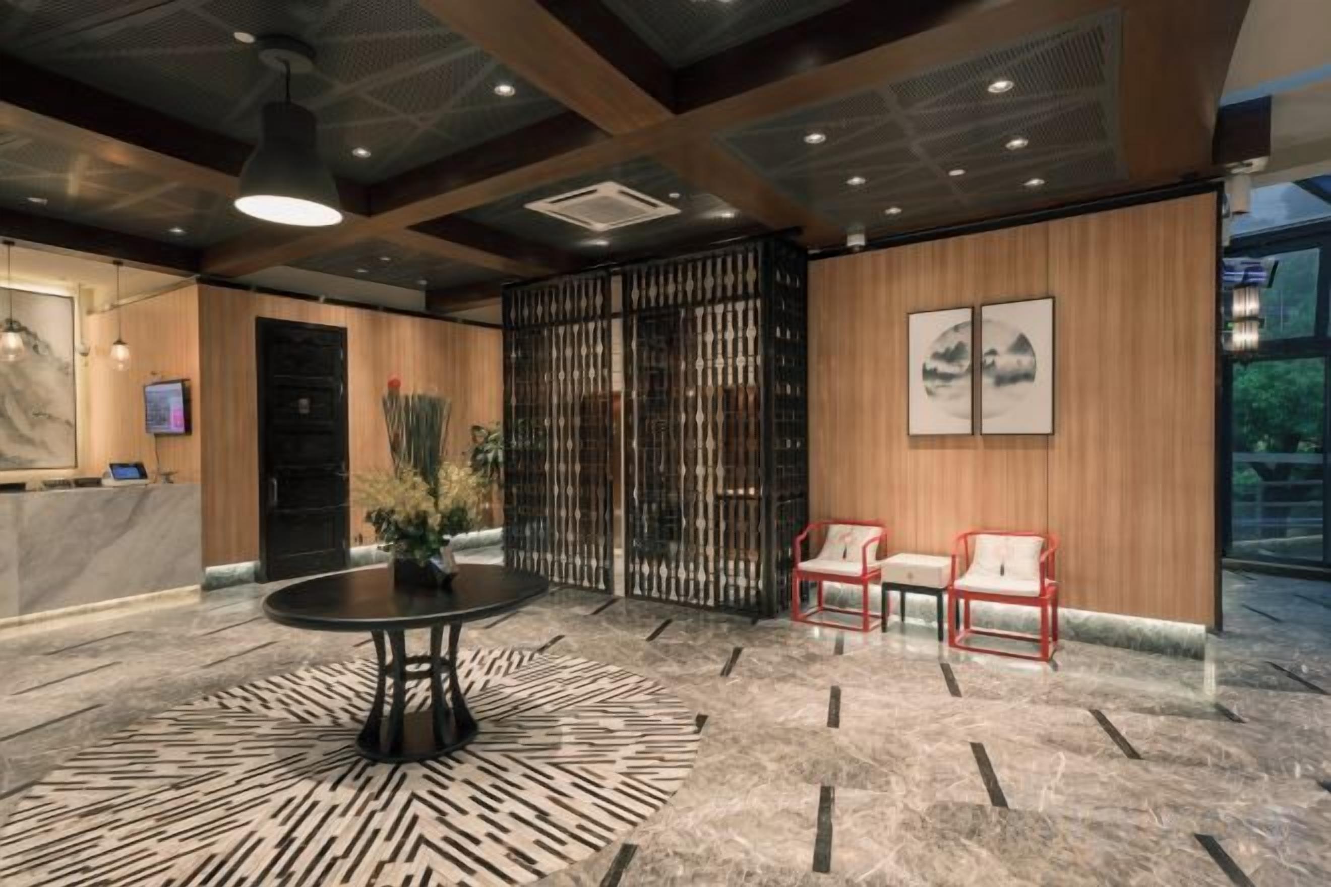 A lobby with a reception desk, a round table, two chairs, a decorative plant, and a large window.