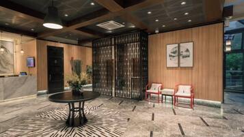 A lobby with a reception desk, a round table, two chairs, a decorative plant, and a large window.