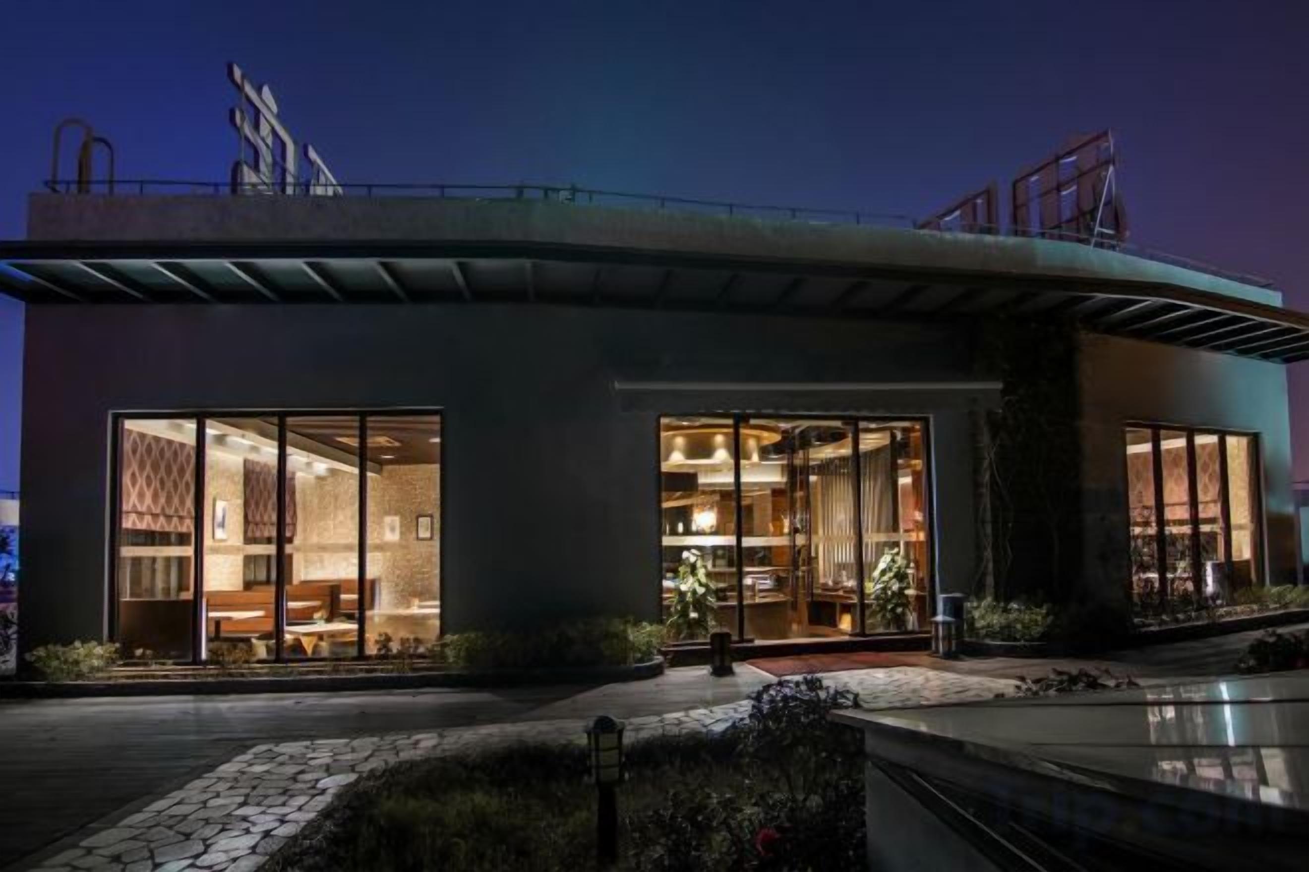 A modern building with large glass windows, a covered entrance, and a rooftop terrace.