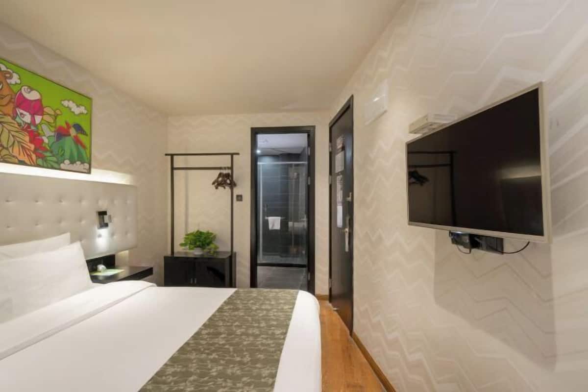 A modern hotel room with a bed, a TV mounted on the wall, a shower area, and a door leading to the bathroom.
