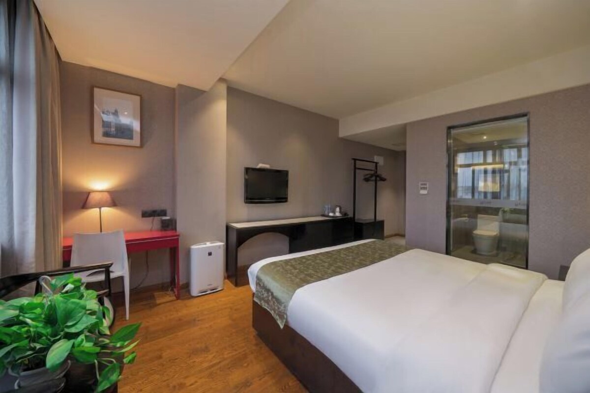 A hotel room with a bed, desk, chair, and a potted plant.