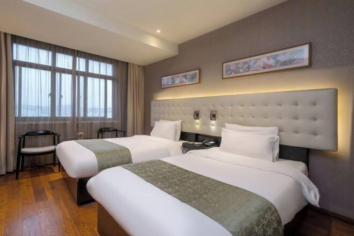 A hotel room with two beds, a large window with curtains, a chair, and two framed pictures on the wall.