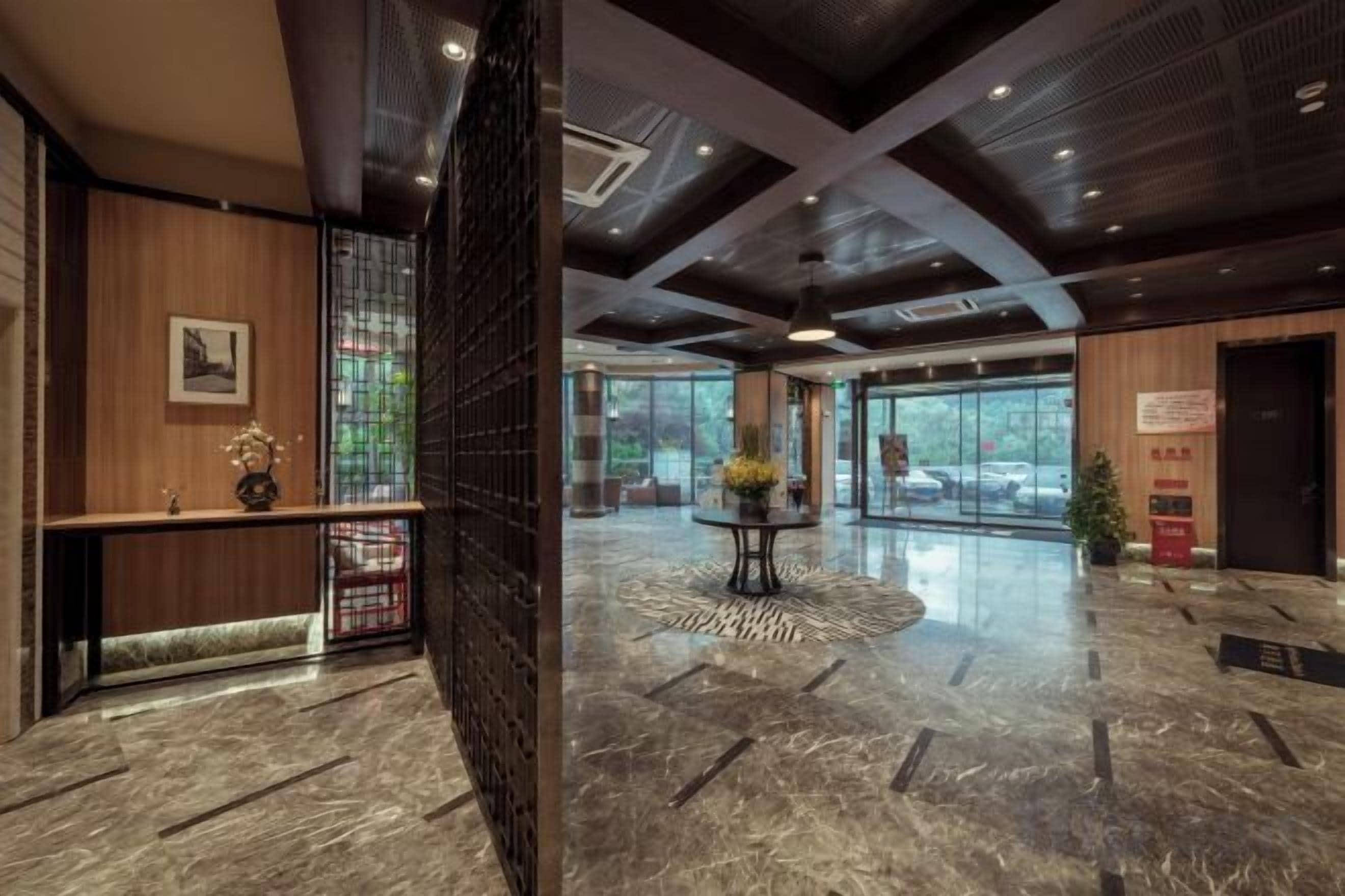 A hotel lobby with a reception desk, a coffee table with flowers, a large window, and a door.