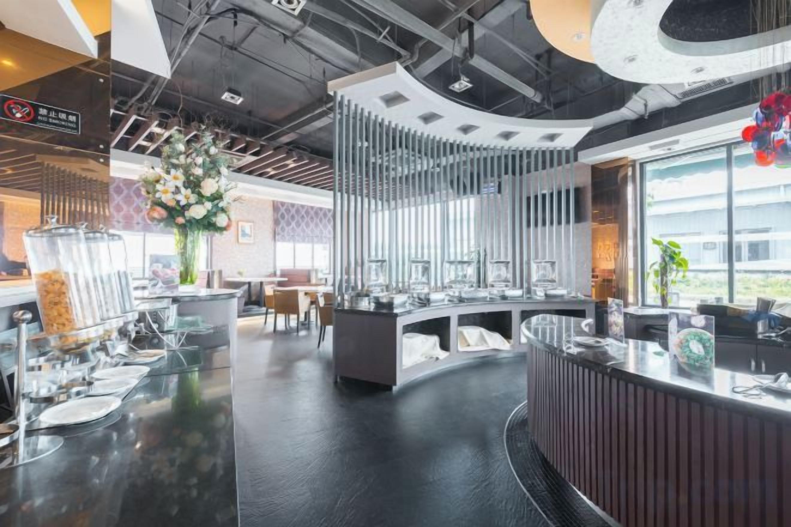 A modern hotel lobby with a curved reception desk, a large flower arrangement, and a view of the outdoors.