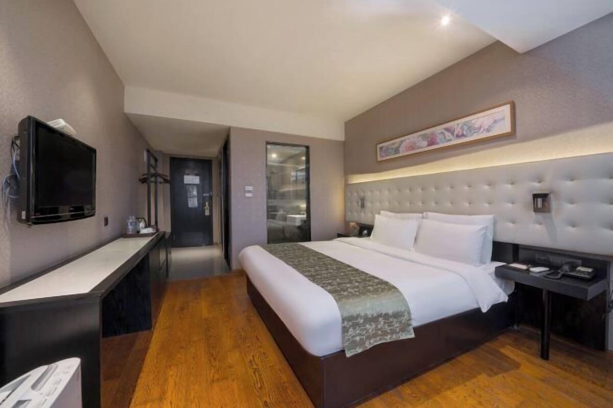A modern hotel room with a large bed, a flat-screen TV, a desk, and a walk-in closet.