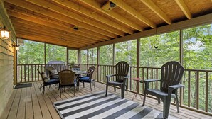 A covered outdoor deck with wooden flooring, a black and white striped rug, and several chairs and a table. - Welcome to “The Love Shack” – Your Perfect Charming Getaway! (Burnside)