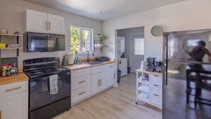 A modern kitchen with white cabinets, a black stove, a microwave, and a refrigerator. - Crater Lake House l Close to Hwy 97 l  OIT l Skylake l Family l Pet Friendly (Klamath Falls)