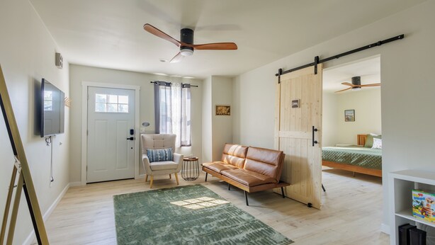 A room with a wooden floor, a green rug, a leather sofa, a chair, a TV, and a sliding door leading to another room. - Crater Lake House l Close to Hwy 97 l  OIT l Skylake l Family l Pet Friendly (Klamath Falls)