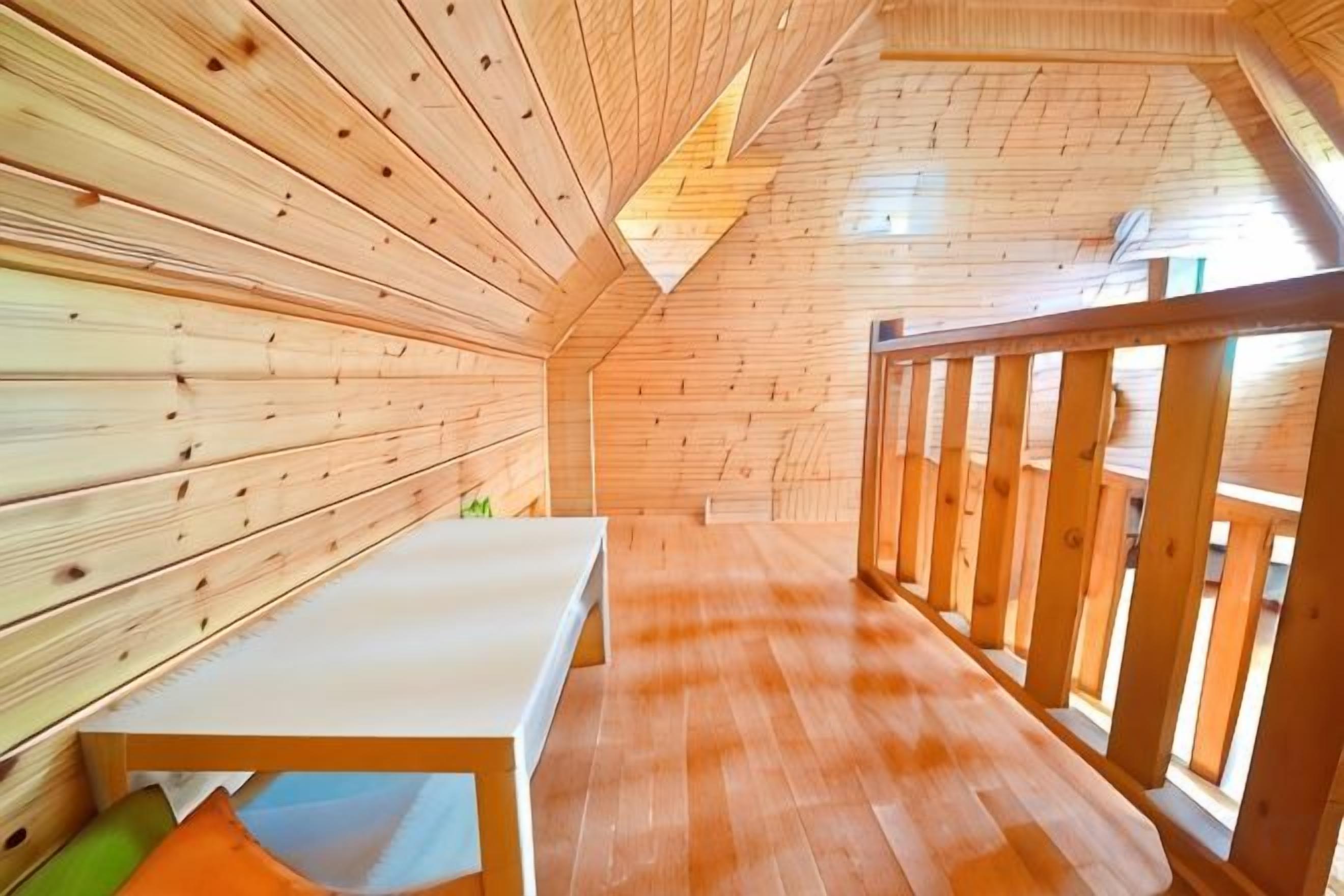 A wooden interior with a sloped ceiling, a bench, and a view through a window.