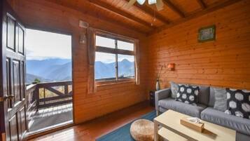 Un intérieur en bois avec un canapé, une table et une vue sur les montagnes par une grande fenêtre.