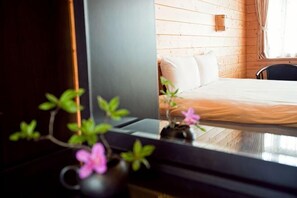 A wooden cabin interior with a bed, a small table with a vase of flowers, and a window with curtains. - Beverly Hills (Nantou)