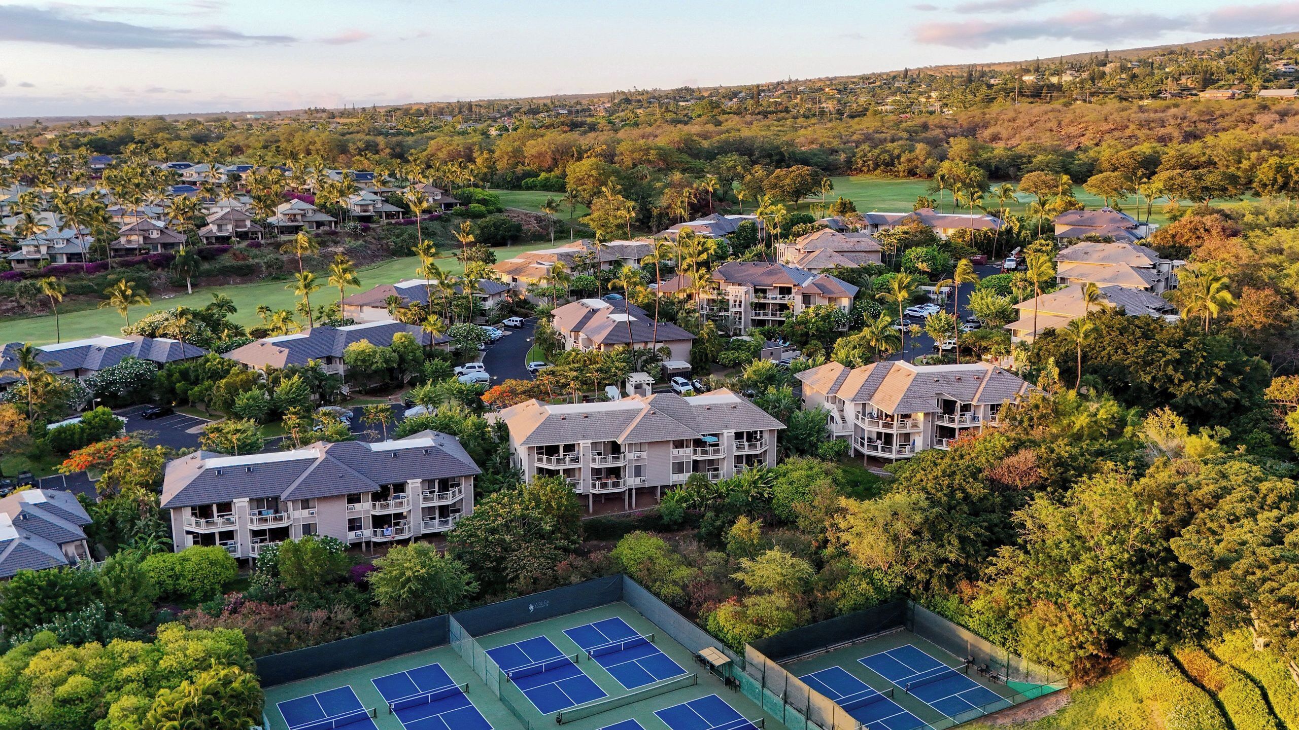A residential area with multiple two-story houses, a tennis court, and surrounding greenery.