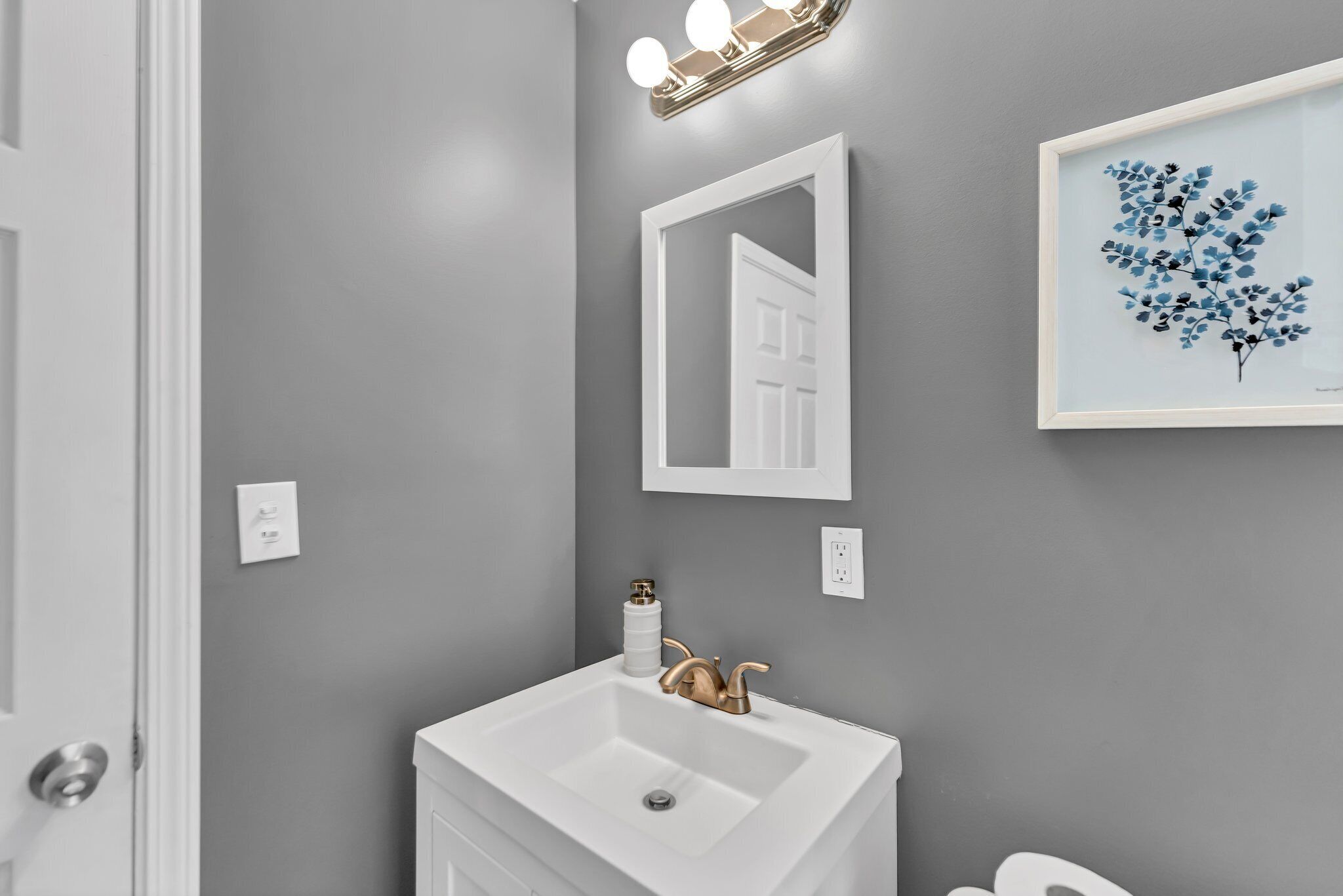 A bathroom with a white sink, a mirror, and a framed artwork on the wall.